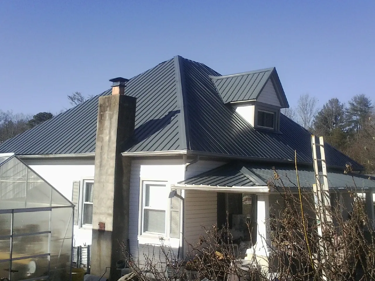 Dark blue standing seam metal roof on a white farmhouse with dormer — Slate & Tile Roof Repair by Roofing Brothers in Coker