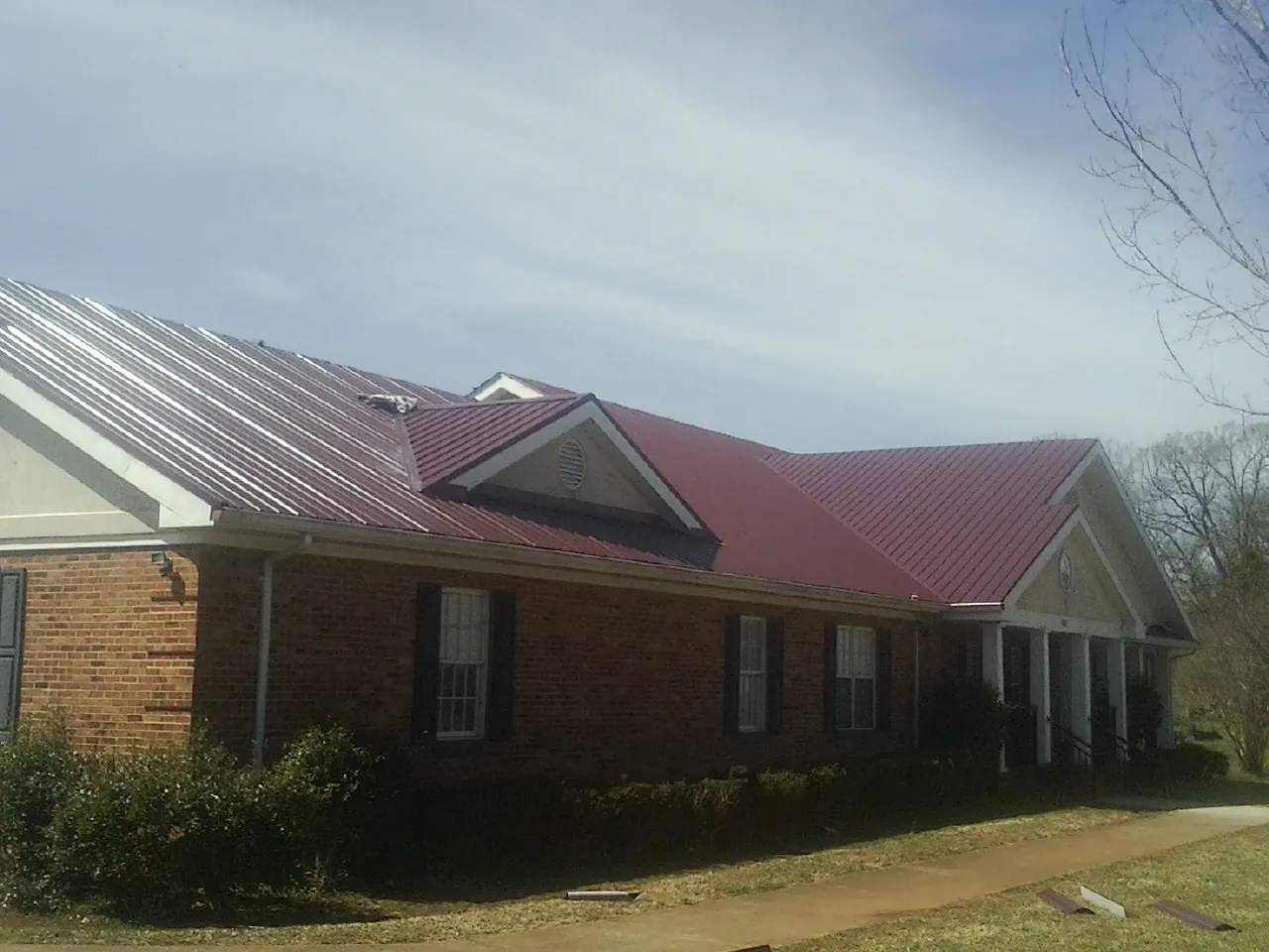 Red metal roof with gabled entries on a long brick building, from a Hail Damage Roof Repair job in Coker