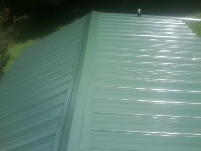 New green metal panels meeting at the ridge of a roof — Flat Roof Repair work by our crew in Coker