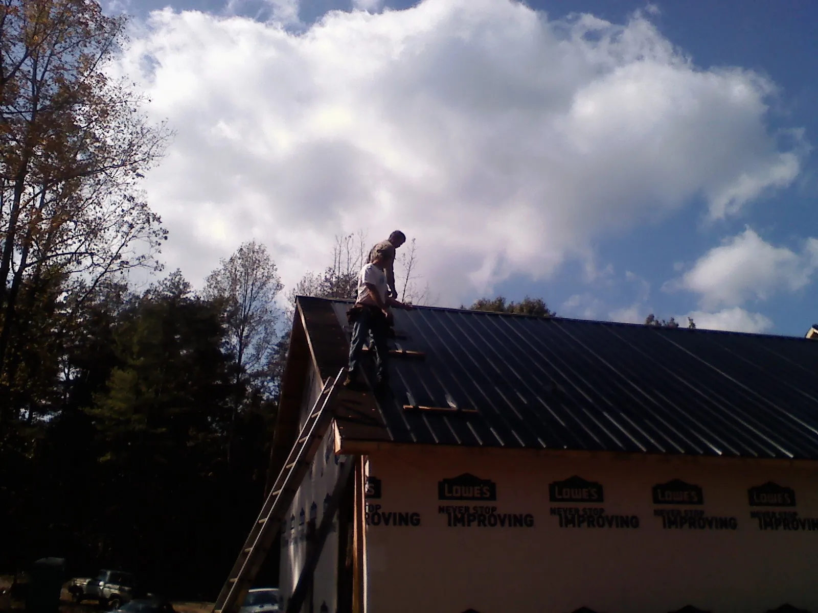 Roofer fastening dark metal panels high against a cloudy sky, from a Roof Inspection job in Coker
