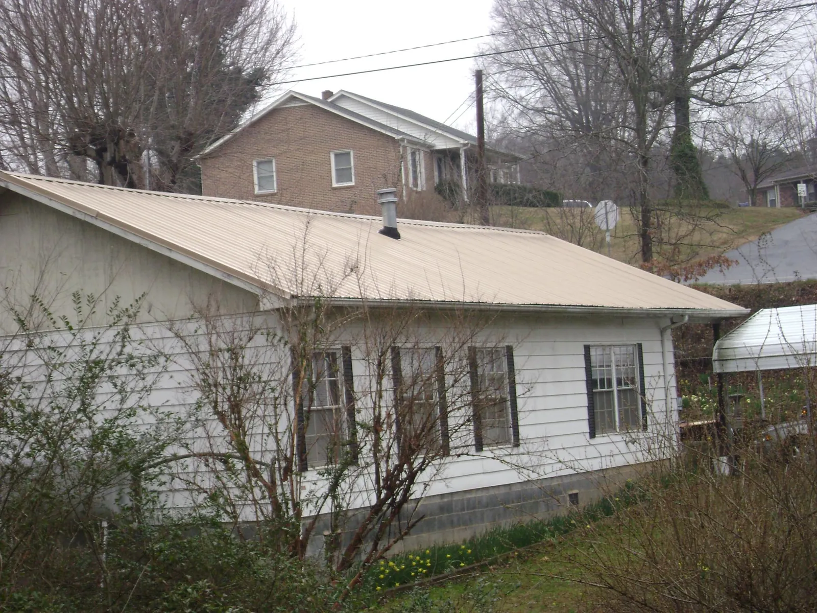 Tan metal roof on a white sided house set into a hillside — Commercial Roofing by Roofing Brothers in Coker