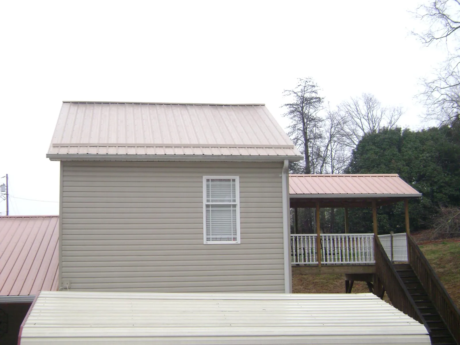 Tan metal roofs on a two story addition and attached porch, from a Roof Replacement job in Coker